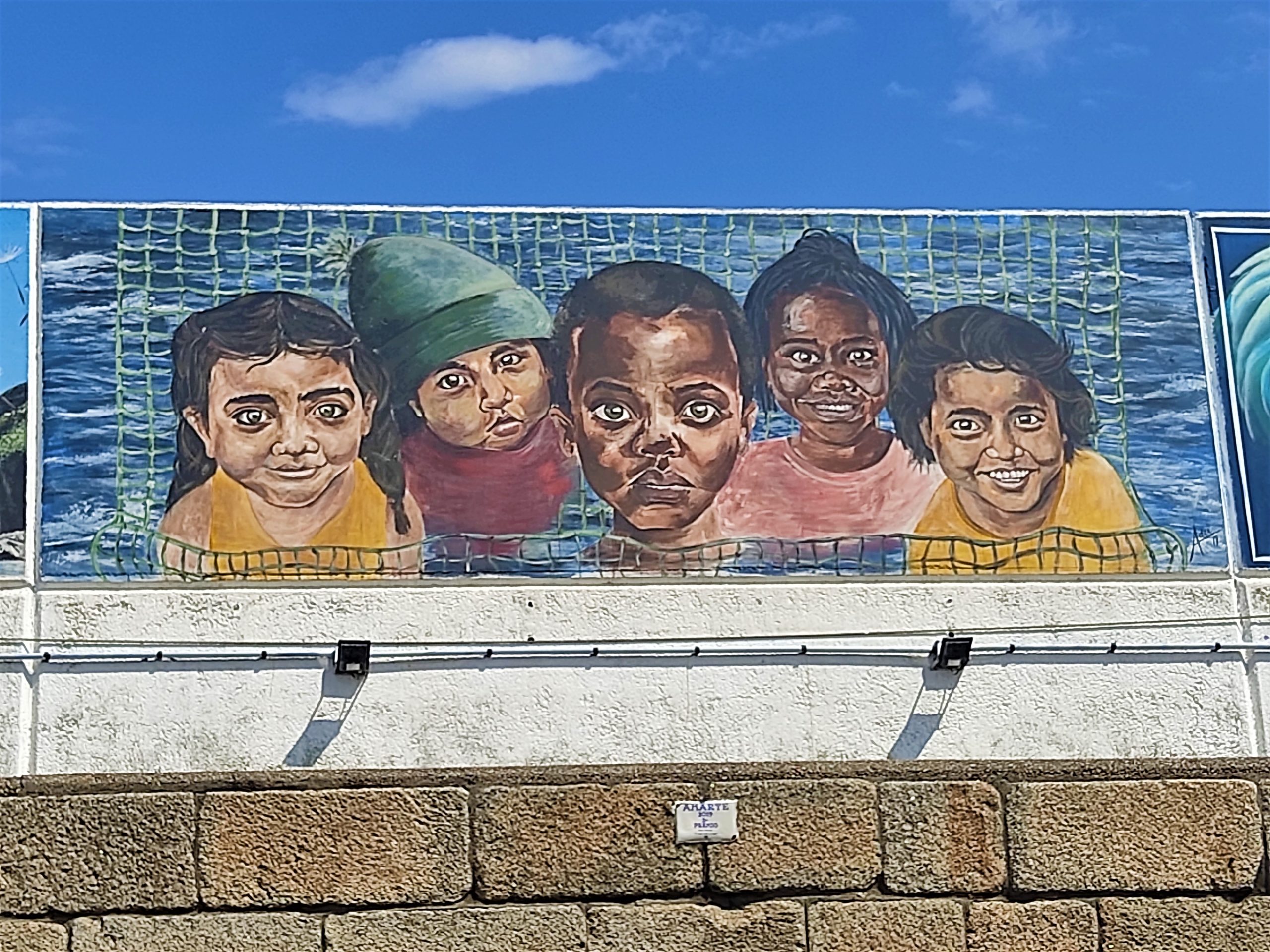 Mural intercultural no porto de Burela con rostros de nenas e nenos de distintas orixes